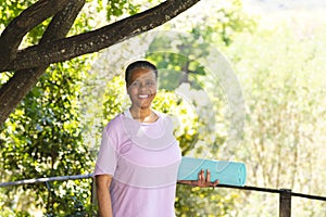 Happy african american senior woman holding exercise mat and smiling in sunny garden, copy space