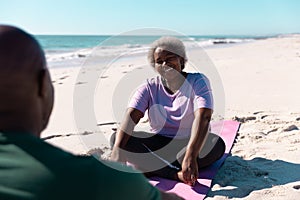 Happy african american senior woman talking with man while relaxing on mats at beach in summer