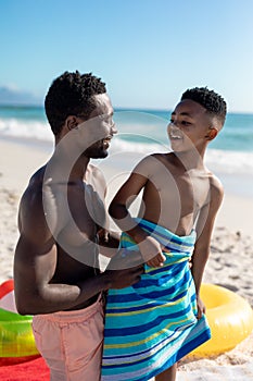 Happy african american shirtless father and son looking at each other on sunny day at beach