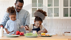 Happy African American sibling kids helping daddy to prepare dinner