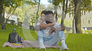 Happy African American sister hugging brother in sunny summer park. Portrait of cheerful siblings looking at camera and