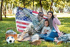 happy african american soldier in military uniform and family holding american flag