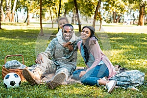 happy african american soldier sitting on grass with family