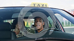 Happy African American taxi driver talking with lady sitting on the backseat. Yellow taxi car roof sign. People, job