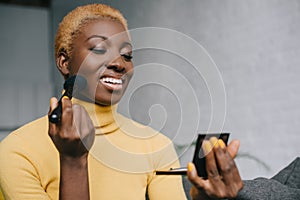 Happy african american woman applying powder photo