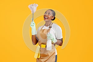 Happy african american woman cleaner dusting using feather duster, studio