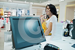 Happy african american woman customer with colored shopping bags paying near cash teminal