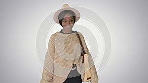 Happy african american woman in hat and knitwear walking with shopping bags on gradient background.