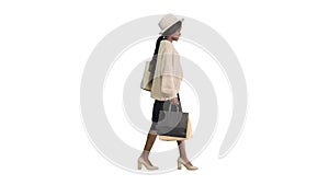 Happy african american woman in hat and knitwear walking with shopping bags on white background.