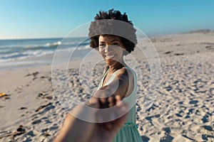 Happy african american woman holding cropped hand of boyfriend at beach on sunny day