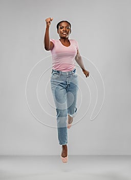 Happy african american woman jumping over grey