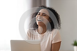 Happy African American woman laughing at funny joke, using laptop