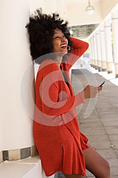 Happy african american woman leaning on wall with mobile phone