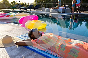 Happy african american woman lying on towel and sunbathing next to swimming pool in garden