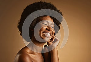 Happy African American woman with a natural afro posing against brown studio copyspace background. Young beautiful black
