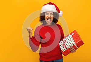 Happy African American woman overjoyed holding christmas gifts and saying YES on orange background, smiles