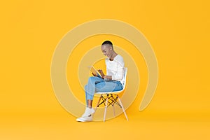 Happy African American woman sitting on a chair using tablet computer in yellow  studio background