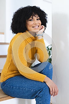 Happy african american woman sitting with hand on face on stairs at home, copy space