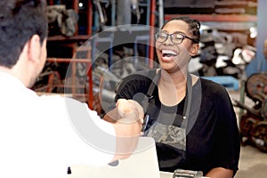Happy African American woman staff with apron making handshake with customer after completing business deal at auto spare parts