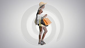 Happy african american woman in straw hat walking with shopping bags on gradient background.