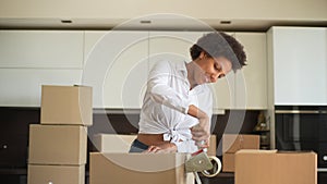 Happy African-American woman using adhesive tape to pack things in cardboard boxes, wrapping carton storage containers