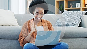 Happy African American woman using laptop and waving on a video call in a living room. Young black female having a