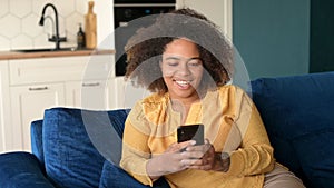 Happy African-American woman using smartphone sitting on the couch