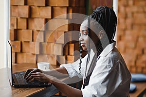 Happy african american woman worker using laptop work study at computer in loft office or cafe, smiling mixed race female student