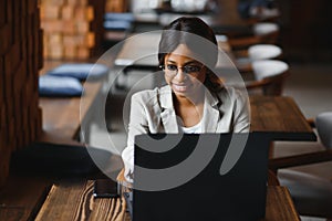Happy african american woman worker using laptop work study at computer in loft office or cafe, smiling mixed race female student