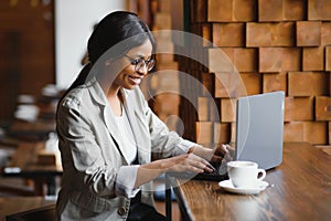 Happy african american woman worker using laptop work study at computer in loft office or cafe, smiling mixed race female student