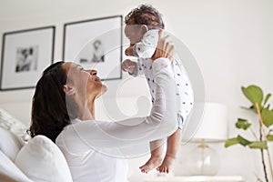 Happy African American  young adult mother raising her three month old baby son in the air, smiling at him, close up, side view