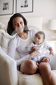 Happy African American  young adult mother sitting on an armchair holding her three month old baby son, smiling to camera, vertica