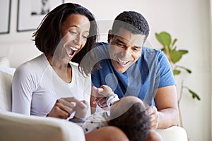 Happy African American  young adult parents playing with their three month old baby son, lying on his motherï¿½s knee, selective f