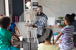 Happy african american young male teacher explaining skeleton to multiracial elementary students