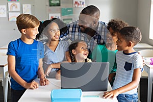 Happy african american young male teacher with multiracial elementary students using laptop