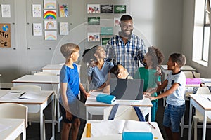 Happy african american young male teacher teaching laptop to multiracial elementary students