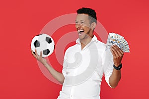 Happy african american young man holding cash money and soccer ball celebrate victory over red background.