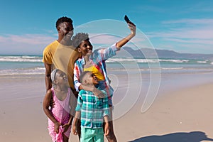 Happy african american young woman taking selfie with man, son, daughter over smartphone at beach