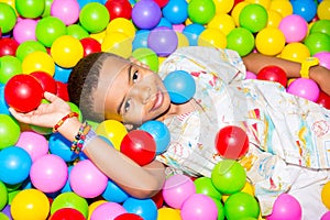 Happy african black boy playing in ball pit on birthday party in kids amusement park and indoor play center. Child