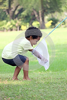 Happy African boy with black curly hair plays fun with scoop-net for catching insect bug and butterfly in green garden. Child