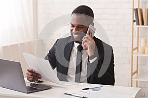Happy african businessman checking reports, talking by phone with assistant