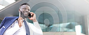 Happy african businessman holding his phone while standing near the building and looking straight ahead