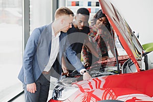 Happy african car salesman showing car engine to customers