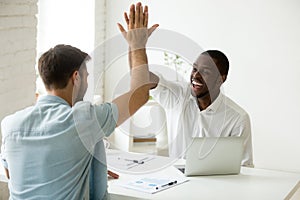 Happy african and caucasian businessmen giving high five in offi