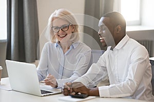 Happy african and caucasian colleagues talking in office at laptop