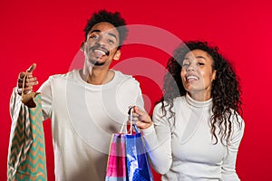 Happy african couple with colorful paper bags after shopping isolated on red