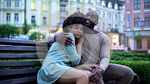 Happy african couple cuddling on bench at sunset, date in city park, closeness