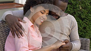 Happy african couple hugging on bench, outdoor date in city cafe, closeness