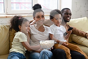 Happy african couple with kids relaxing at home watching tv