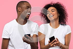 Happy african couple laughing using smartphones isolated on pink background photo